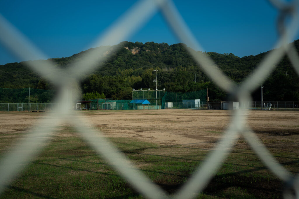 SONY α7C IIと SIGMA 45mm F2.8 DG DNで撮影したフェンス越しの山をバックした野球グラウンド